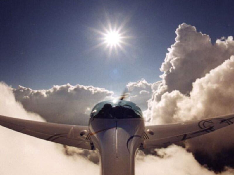 Vue avant d'un ULM volant au-dessus des nuages avec un soleil éclatant dans un ciel bleu clair.